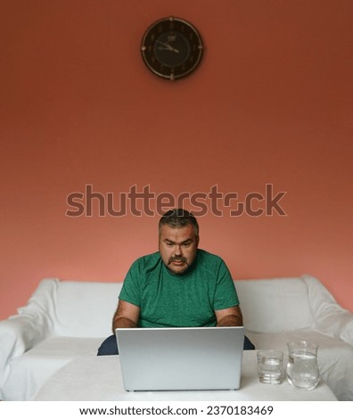 middle age freelancer Businessman at home using laptop on table on pink wall background. business man looking at screen of computer. one, alone bearded male hard working at home. green t-shirt
