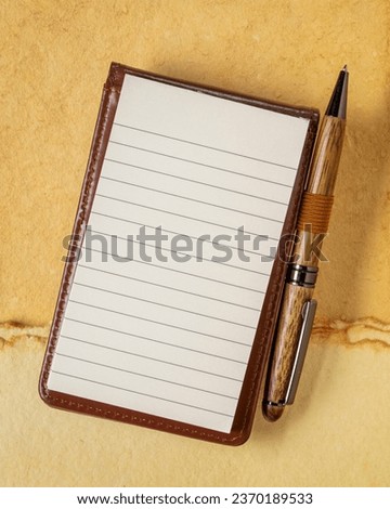 blank sheet of ruled paper in a small journal with a luxury pen against textured art paper