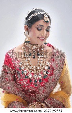 This photograph showcases a stunning Indian bride adorned in traditional attire, radiating grace and elegance while posing for a picture. The bride’s ensemble includes ornate jewelry, makeup