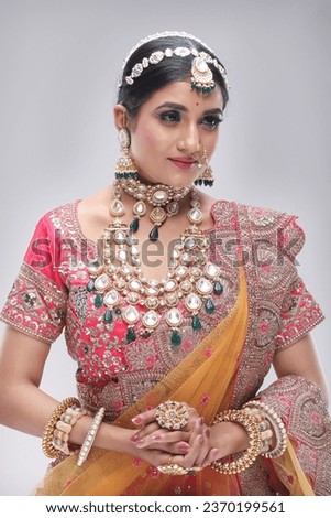 This photograph showcases a stunning Indian bride adorned in traditional attire, radiating grace and elegance while posing for a picture. The bride’s ensemble includes ornate jewelry, makeup
