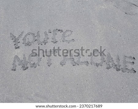 The writing you're not alone on the beach sand background.
