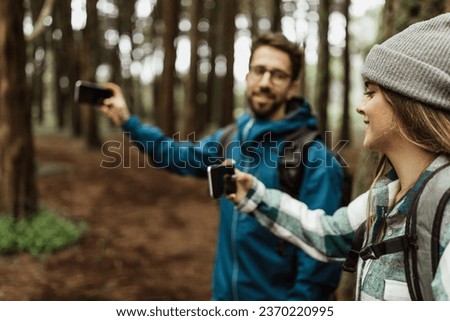 Smiling young caucasian family in jackets taking photo on phone with empty screen, enjoy adventure at weekend, walk in cold forest in autumn. Device for vacation together, active lifestyle