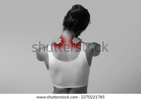 Neck pain muscle stress and strain. Unrecognizable stressed woman wearing white top massaging red sore neck highlighted in red, back view, black and white photo, copy space