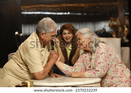 Indian happy senior couple playing arm wrestle game at living room. Concept : Happy Family Lifestyle theme.