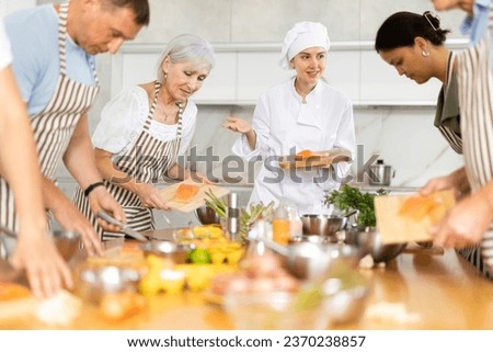 Serious young woman chef of cooking course teaching attendees how to cook salmon fish Royalty-Free Stock Photo #2370238857