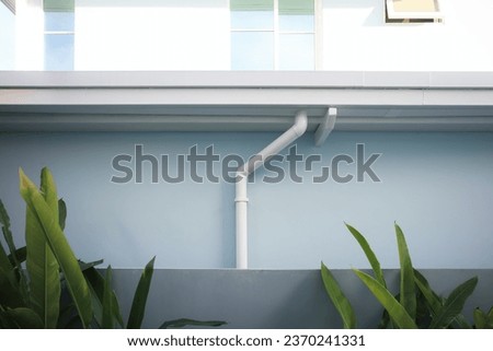 Rain gutter install on steel structure, connect to pvc downpipe or downspout, elbow at eaves, exterior house building. Also called guttering or eavestrough for water drainage system. Look new clean. Royalty-Free Stock Photo #2370241331