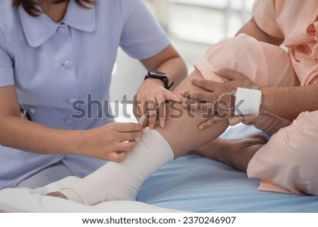 Close-up of female nurse bandaging foot of elderly woman patient at the hospital