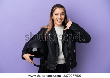 Young caucasian woman holding a motorcycle helmet isolated on purple background making phone gesture. Call me back sign