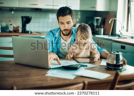 Young father embracing his daughter while paying bills in the kitchen Royalty-Free Stock Photo #2370278111