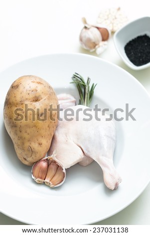 Uncooked duck leg on a white plate with garlic, potato and spices