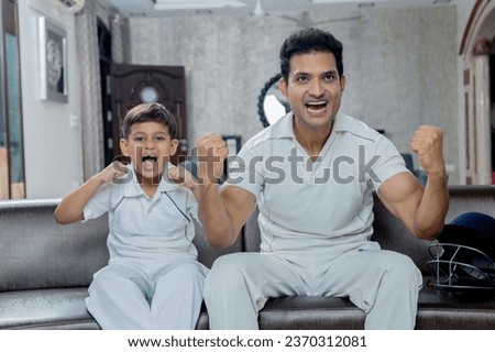 Indian Father and son in cricket dress watching cricket and supporting cricket team from home, Father son enjoying cricket