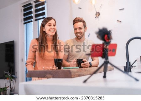 Influencer couple recording video with phone for social media network sitting at home with a coffee cup