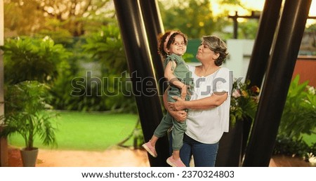 Happy Indian old grandmother holding cute little child girl in arms hands whirl dancing together outdoor home. Beautiful smiling woman sing song spinning small kid daughter enjoying summer holiday Royalty-Free Stock Photo #2370324803
