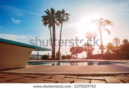 Close-up of a diving board over the open swimming pool during warm light through south palm trees on hot summer day Royalty-Free Stock Photo #2370329753