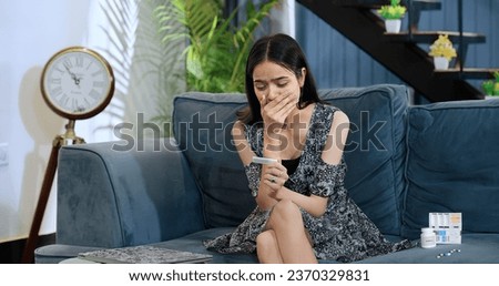Worried depressed Indian teen girl sitting on sofa hold pregnancy test stick received negative results after IVF at home. Stressed pregnant female feel sad look upset for unplanned baby regret mistake Royalty-Free Stock Photo #2370329831