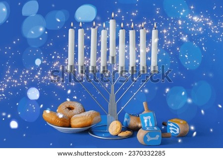 Glowing candles, dreidels, donuts and cookies for Hannukah celebration on blue background Royalty-Free Stock Photo #2370332285