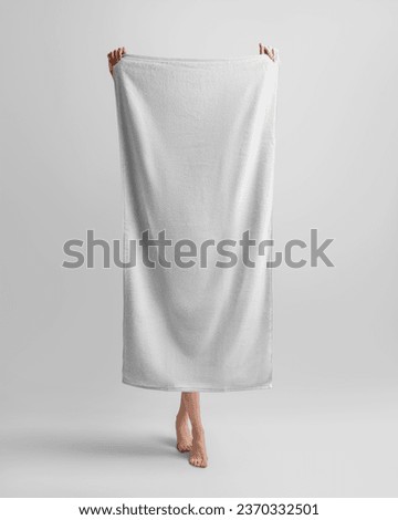 A mockup of a white bath towel, a girl holds it in her hands, in full height, her legs are visible. Template of textured soft towelette isolated on background. Personal hygiene product for dry body.  Royalty-Free Stock Photo #2370332501
