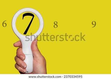 The number 7 seen enlarged through a magnifying glass. On a Yellow background with plenty of copy space. 