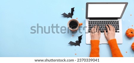 Female hands with laptop, cup of coffee and Halloween decor on blue background with space for text