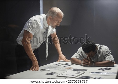 Portrait of senior detective interrogating young Black man in police station
