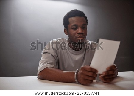Portrait of Black young man looking at picture of evidence in police station
