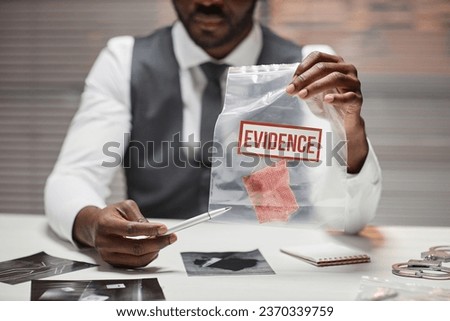 Close up of Black male detective holding plastic bag with evidence during interrogation of suspect, copy space
