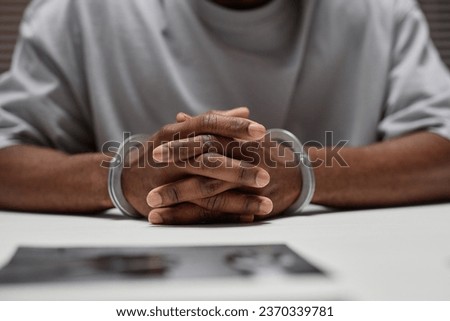 Close up of anonymous black man wearing handcuffs sitting at table in police department with hands clasped, copy space