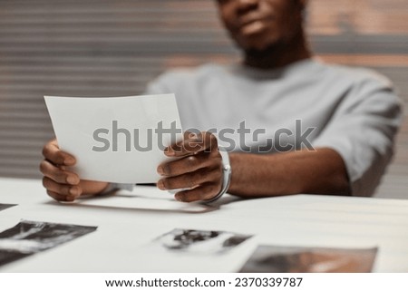 Close up of African American man wearing handcuffs looking at pictures in police department, copy space