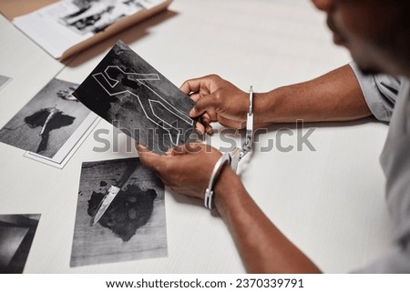 Closeup of man wearing handcuffs looking at evidence pictures during interrogation in police department, copy space