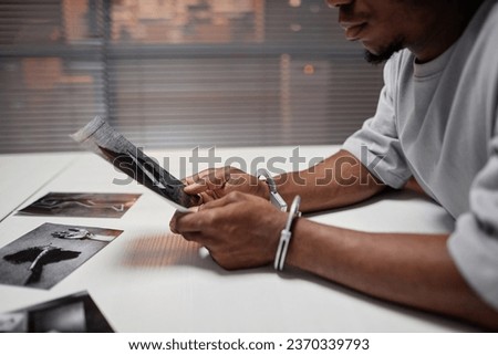 Side view closeup of criminal wearing handcuffs looking at evidence pictures during interrogation in police department, copy space