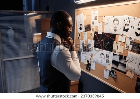 Side view detective looking at evidence board in office and thinking while investigating case, copy space Royalty-Free Stock Photo #2370339845