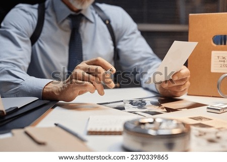 Close up of male detective holding picture of evidence in office and smoking cigarette, copy space