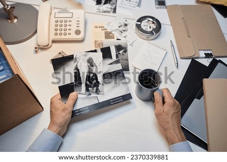 Top view closeup of male detective with hands holding pictures of evidence at desk, copy space