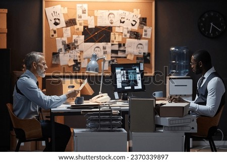 Side view portrait of two police detectives sitting at desk in office on opposite sides studying case investigation Royalty-Free Stock Photo #2370339897