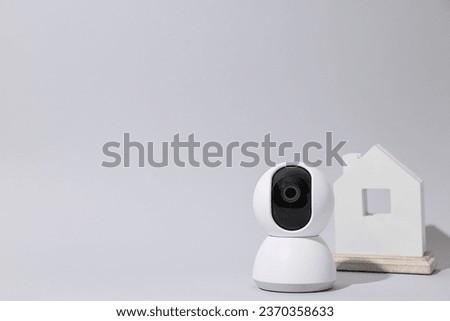 Wooden house and home security camera on gray background, space for text