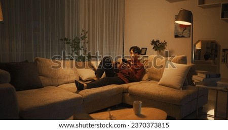 Portrait of a Stylish South Korean Man Shopping Online on His Smartphone While Resting on a Couch in a Comfortable Living Room. Asian Male Entering Credit Card Details into Mobile E-Commerce App Royalty-Free Stock Photo #2370373815