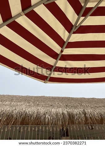 Vintage roof made from dry palm leaf and striped beach umbrellas on blue sky background. Banner design