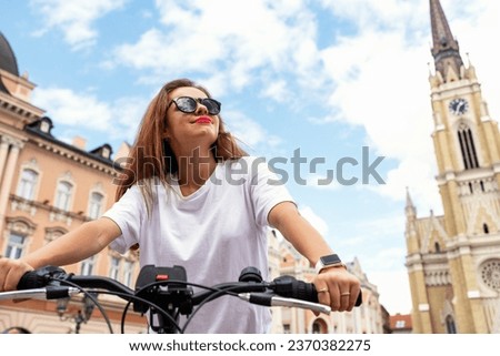 Brunette woman wearing sunglasses riding a bike, bicycle travel tour around historic place in Novi Sad, Serbia.