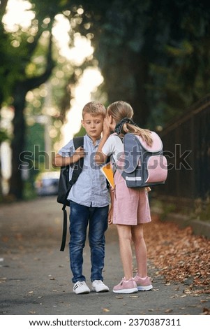 To gossip. Young school children of boy and girl are together outdoors.