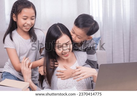Asian family mother daughter cute son spending time play together while working on laptop technology computer in living room, cheerful kids expresss love kiss mom relaxation parenthood multitasking
