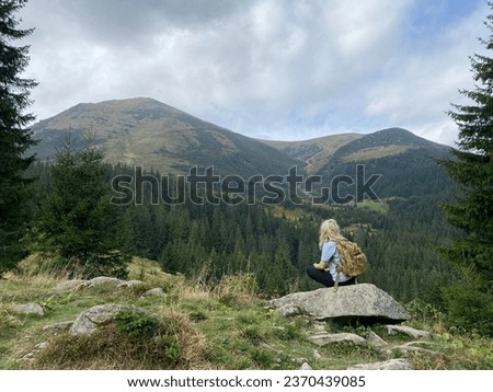 While traveling in the mountains, the girl stops with a large backpack to enjoy the scenery.