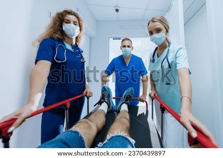 Three doctors of different genders are rolling a gurney with a patient in the hospital corridor. Emergency medical care. Selective focus on the male doctor.