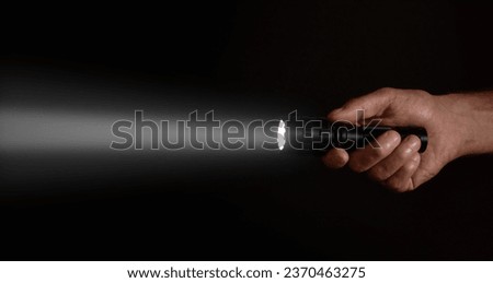 Male hand holding a led flashlight with a wide white beam on a black background, leaving the right side of the frame. Royalty-Free Stock Photo #2370463275