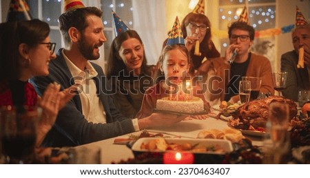 Family Celebrating Birthday with a Young Girl. Father is Holding a Celebratory Cake, Little Daughter is Blowing Out Candles and Making a Joyful Wish. Happy Child is Surrounded by Her Close Relatives