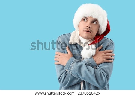Frozen young man in Santa hat on blue background