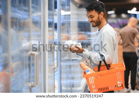 Portrait of handsome young Indian man standing at grocery shop or supermarket, Closeup. Selective Focus