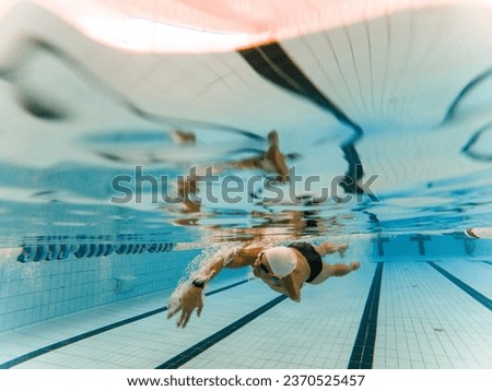 Underwater photo of an adult man with an amputated arm swimming in an indoor pool. The athlete is crawling with only one arm. Disabled swimmers, athletes with an amputated arm. Royalty-Free Stock Photo #2370525457