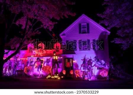 Night photo. Glowing Halloween decorations - skeletons, witches, pumpkins around a small wooden house.