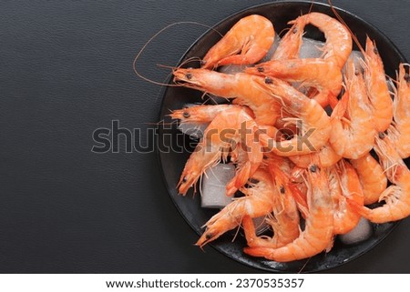 Chilled shrimp in a plate with ice on a dark background. Boiled shrimp in a black plate with ice, top view. Seafood on crushed ice. Healthy eating concept