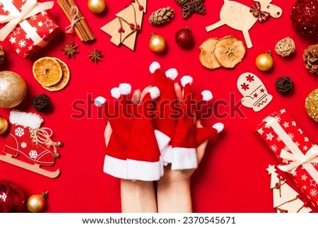 Top view of female hands holding a stack of santa hats on red background. New year decorations. Christmas holiday concept.